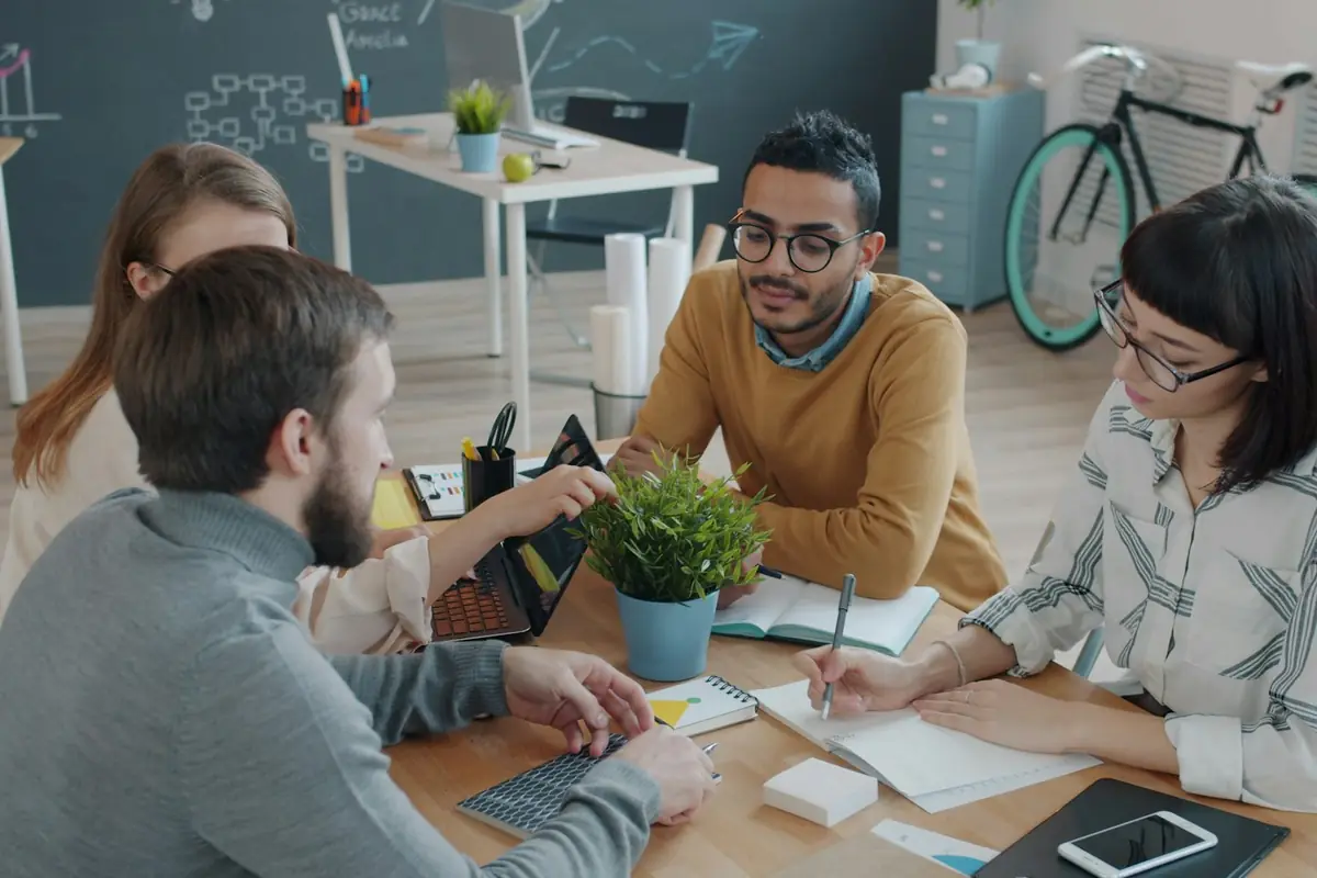 Quatre personnes autour d'une table de travail, carnets et ordinateur ouverts